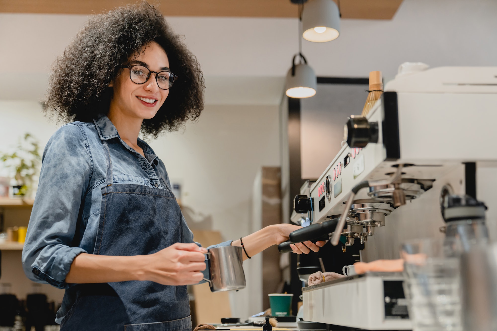 African beautiful young barista making coffee with the help of coffee machine in coffee shop